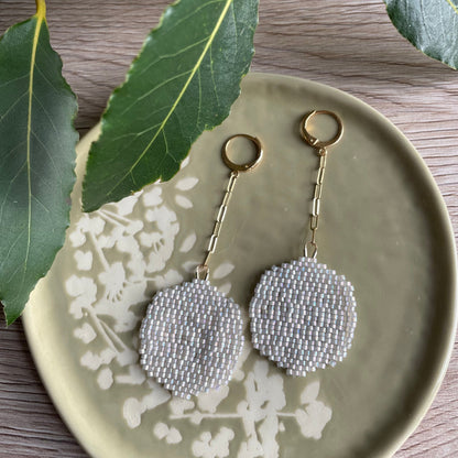 Pair of silver beaded earrings on a decorative plate with green leaves.
